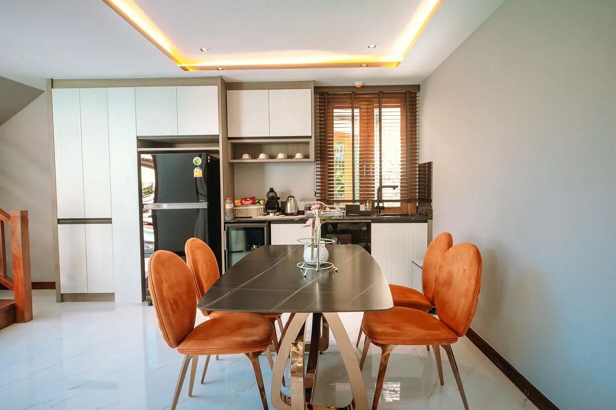 A modern kitchen with white cabinets, a black countertop, and a dining area with a black table and orange chairs.