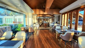 A spacious restaurant with wooden flooring and modern furniture, large windows offering views of the outdoors, and a central bar area. - Yotaka Khanom (Khanom)
