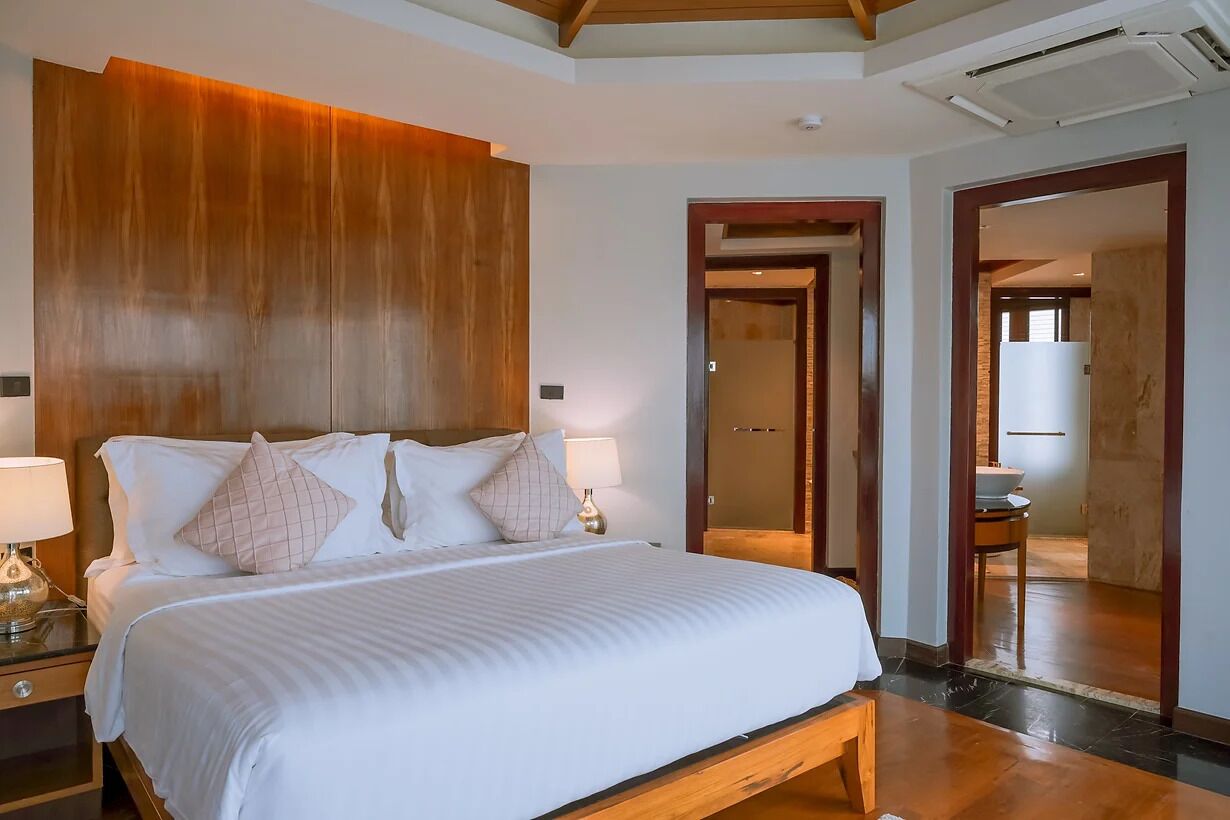 A hotel room with a large bed, wooden headboard, two bedside lamps, and a wooden floor.