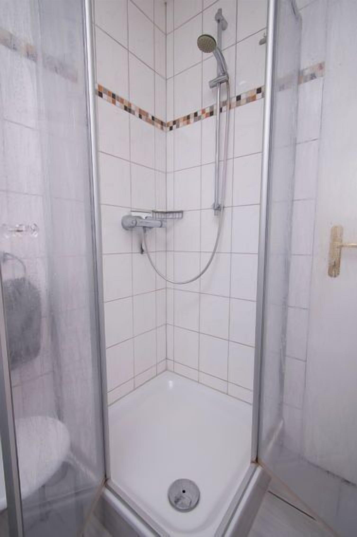 Una doccia con porta in vetro, pavimento piastrellato e soffione.