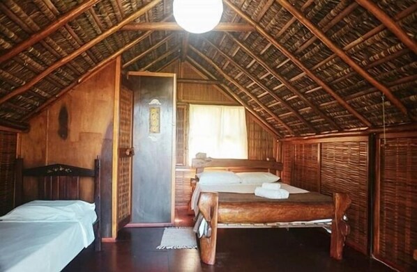 Une pièce rustique en bois, avec un plafond en pente, un lit, une petite table et une porte donnant sur une autre pièce.