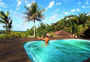 Une piscine où se trouvent deux personnes, entourée de palmiers et bordée d’une terrasse en bois.
