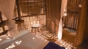 Una habitación con una cama, un taburete pequeño y una ventana con persianas de bambú.