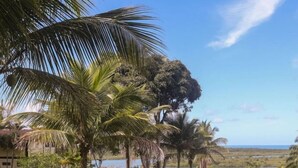 Paisaje tropical con palmeras, una cabaña de techo de paja y vistas a un lago.