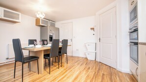 A modern kitchen with white cabinets, a built-in oven, and a dining area with a wooden table and four chairs. - 5 bed house with free secure parking in pleasant quiet location (Wolverhampton)