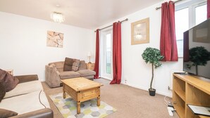 A modern living room with a sofa, a coffee table, a TV, and a potted plant. - 5 bed house with free secure parking in pleasant quiet location (Wolverhampton)