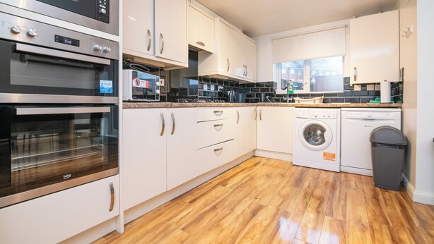 A modern kitchen with stainless steel appliances, white cabinetry, and a wooden floor. - 5 bed house with free secure parking in pleasant quiet location (Wolverhampton)