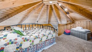 Una camera da letto con soffitto in legno, un letto con copriletto, un comodino e una valigia.