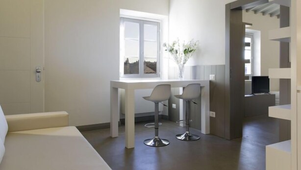 Une chambre moderne et minimaliste, comprenant un lit, une petite table avec deux chaises, une fenêtre donnant sur un beau paysage et un vase avec des fleurs.