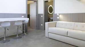 Une pièce moderne et minimaliste, avec un canapé blanc, un coin bar doté de tabourets et un grand miroir.