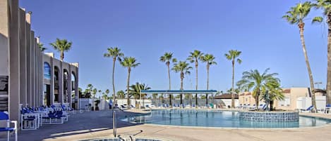 A pool area with lounge chairs, palm trees, and a building with columns.