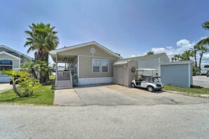 A single-story mobile home with a covered porch, a small attached garage, and a golf cart parked in front. - Deck & Pool Access: Long Island Village Escape! (Port Isabel)
