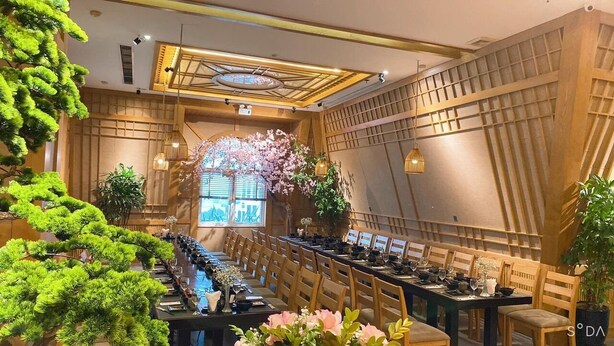 Une longue table à manger, entourée de chaises, de plantes en pot et d’une arche décorative ornée de fleurs.