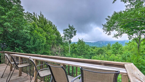Une terrasse en bois, agrémentée de chaises et d’une table, qui offre une vue sur une zone boisée avec des montagnes à l’horizon.