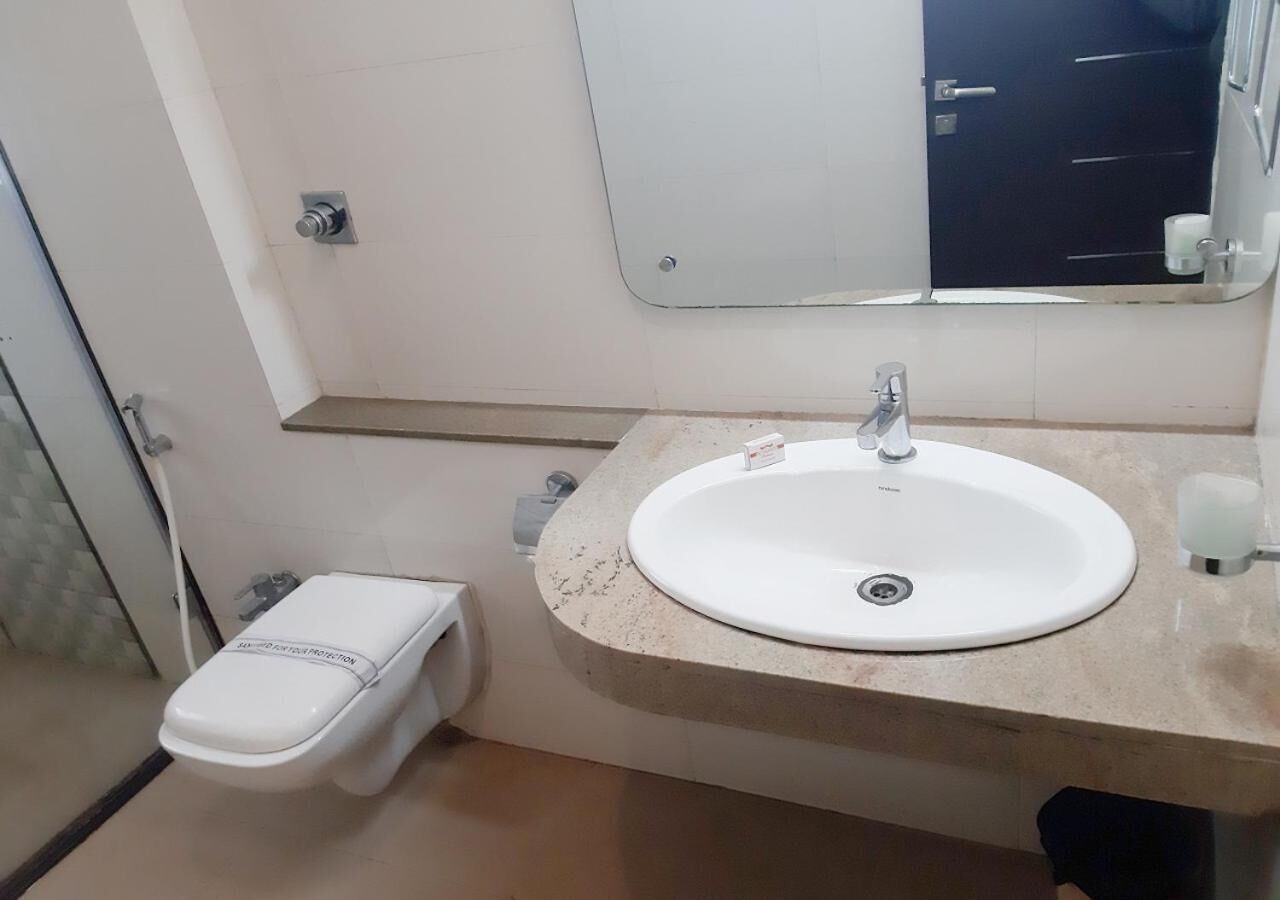 Un baño con inodoro blanco, lavamanos con espejo y dispensador de toallas.