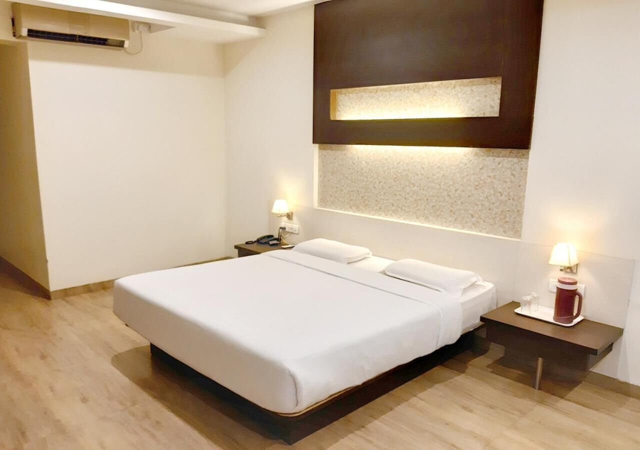 Quarto de hotel moderno com uma cama grande, mesas de cabeceira e luminária fixada na parede.
