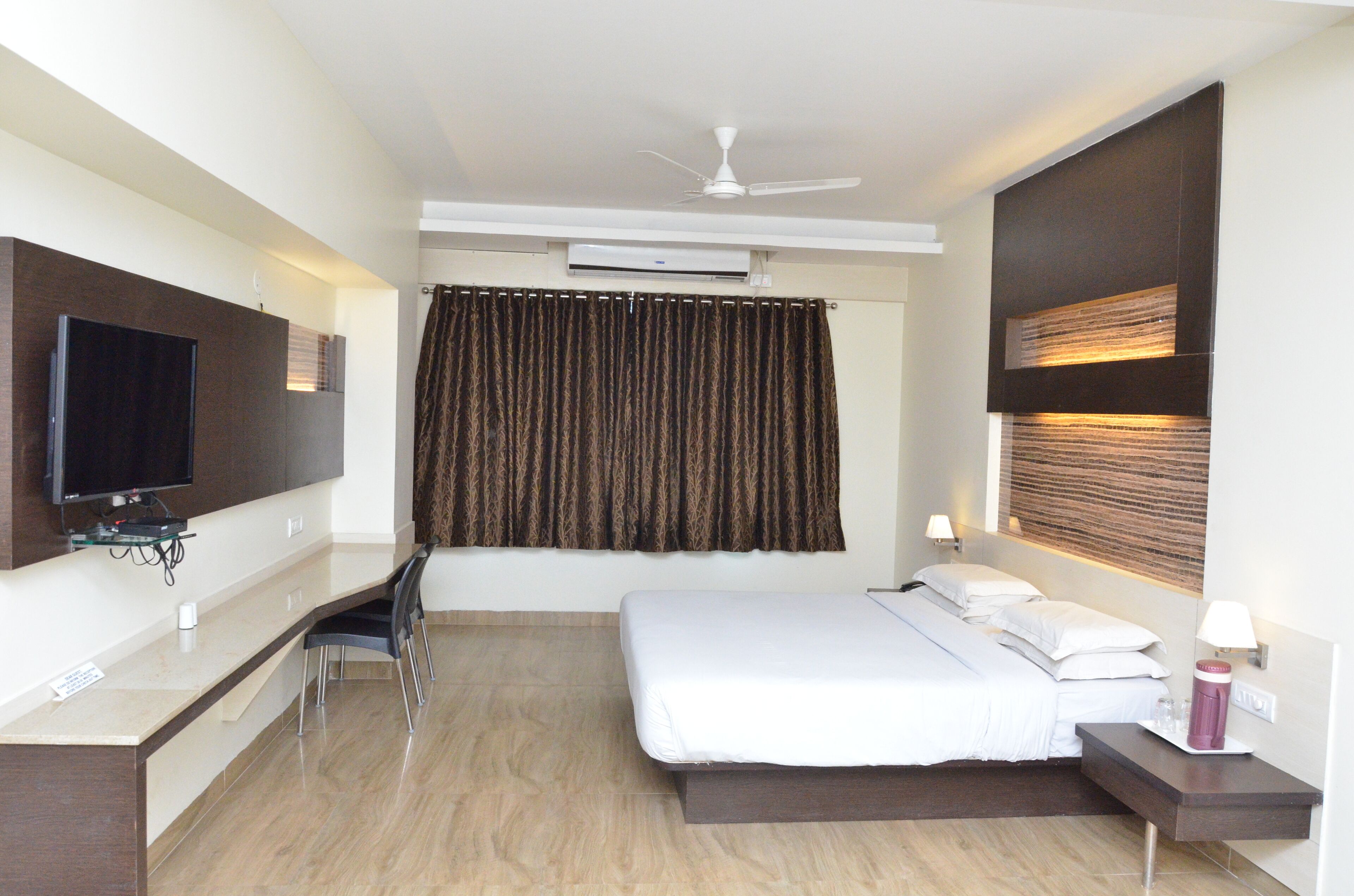 A hotel room with a bed, a desk, a chair, a television, and a ceiling fan.