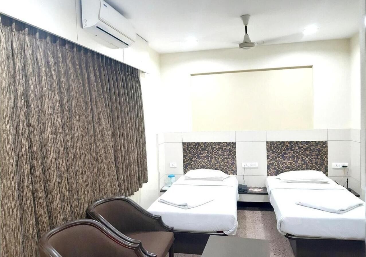 Una habitación de hotel con dos camas individuales, un escritorio, una silla y un amplio ventanal con cortinas.