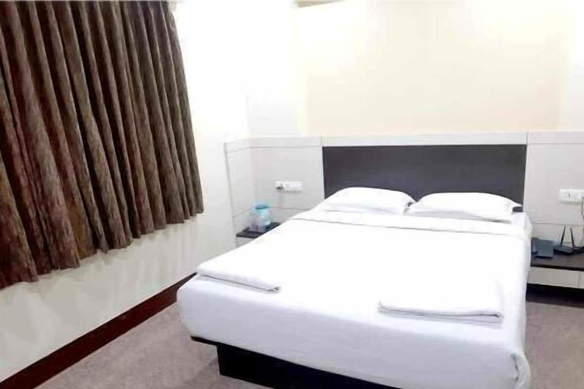 Habitación de hotel con cama, cortinas, mesita de noche y toma de corriente.
