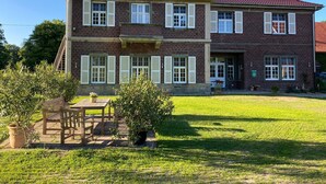 A two-story brick house with a red-tiled roof, white shutters, and a well-maintained lawn.