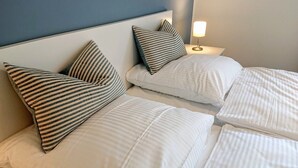 A hotel room with two beds, striped pillows, a nightstand with a lamp, and a blue wall.