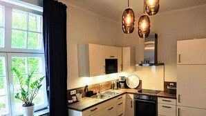 A modern kitchen with white cabinets, a stainless steel sink, and a built-in oven. There is a window with a view of greenery outside.