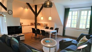 A modern living room with a sofa, a coffee table, and a TV. There is a kitchen area with a dining table and chairs.