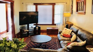 Un salon avec un téléviseur, un canapé, une table basse et une fenêtre avec des rideaux.