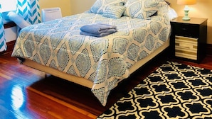 Une chambre à coucher bien rangée, avec un lit, une table de chevet sur laquelle se trouve une lampe, un tableau accroché au mur et un tapis à motifs.