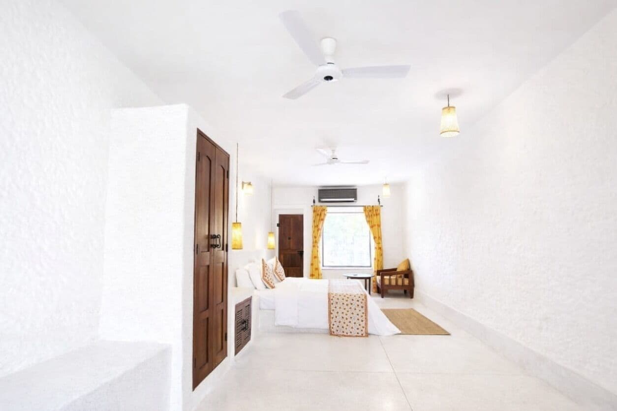 A hotel room with a bed, a desk, a chair, a window with curtains, and a ceiling fan.
