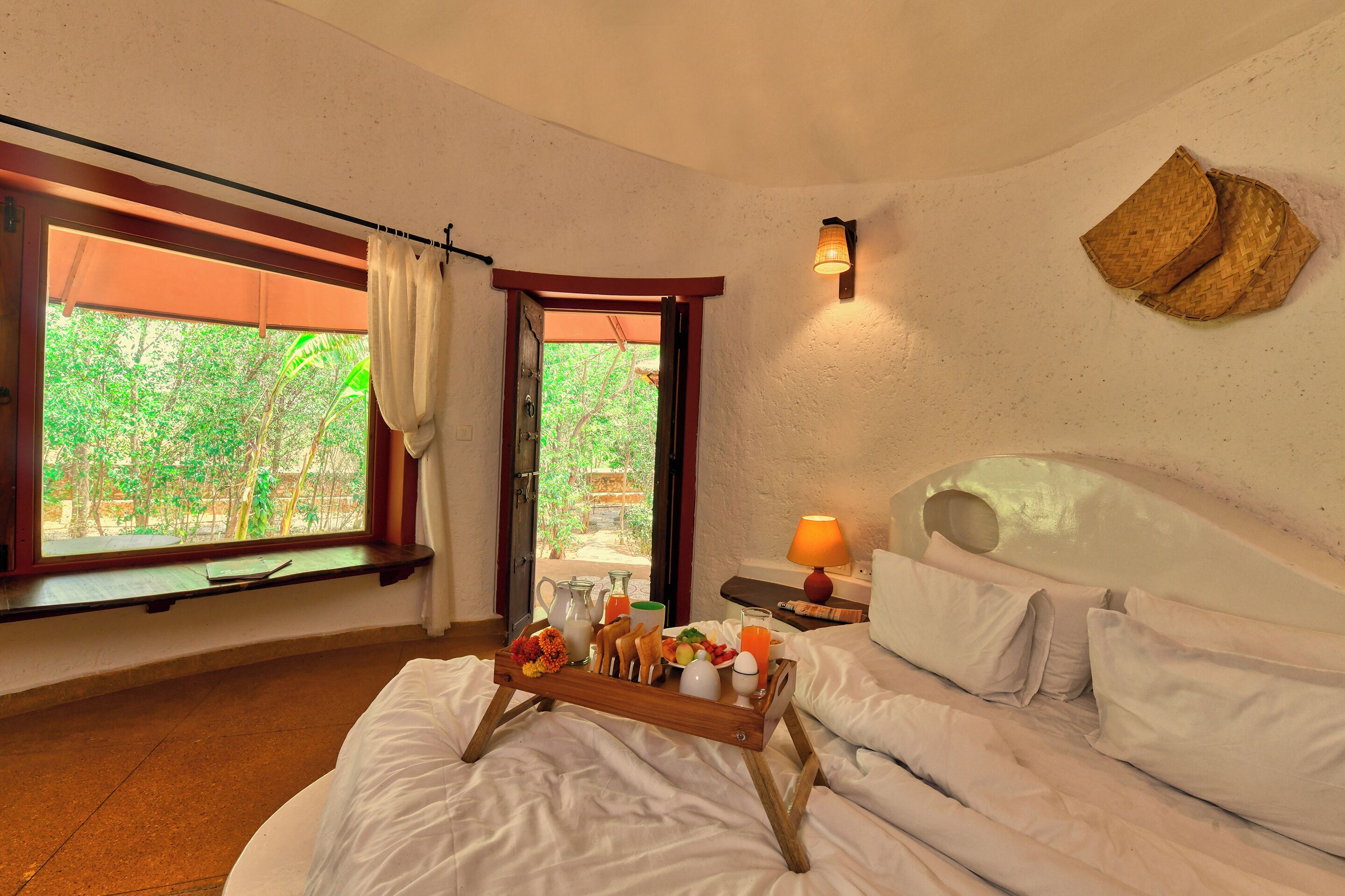 A bedroom with a bed, a tray with breakfast items, a window with curtains, and a wall-mounted lamp.