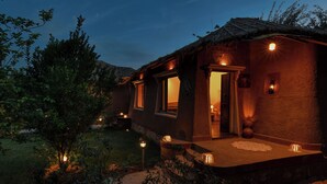 A rustic building with a thatched roof, illuminated windows, and a small porch area. - The Earth At Ranthambore (Sawai Madhopur)