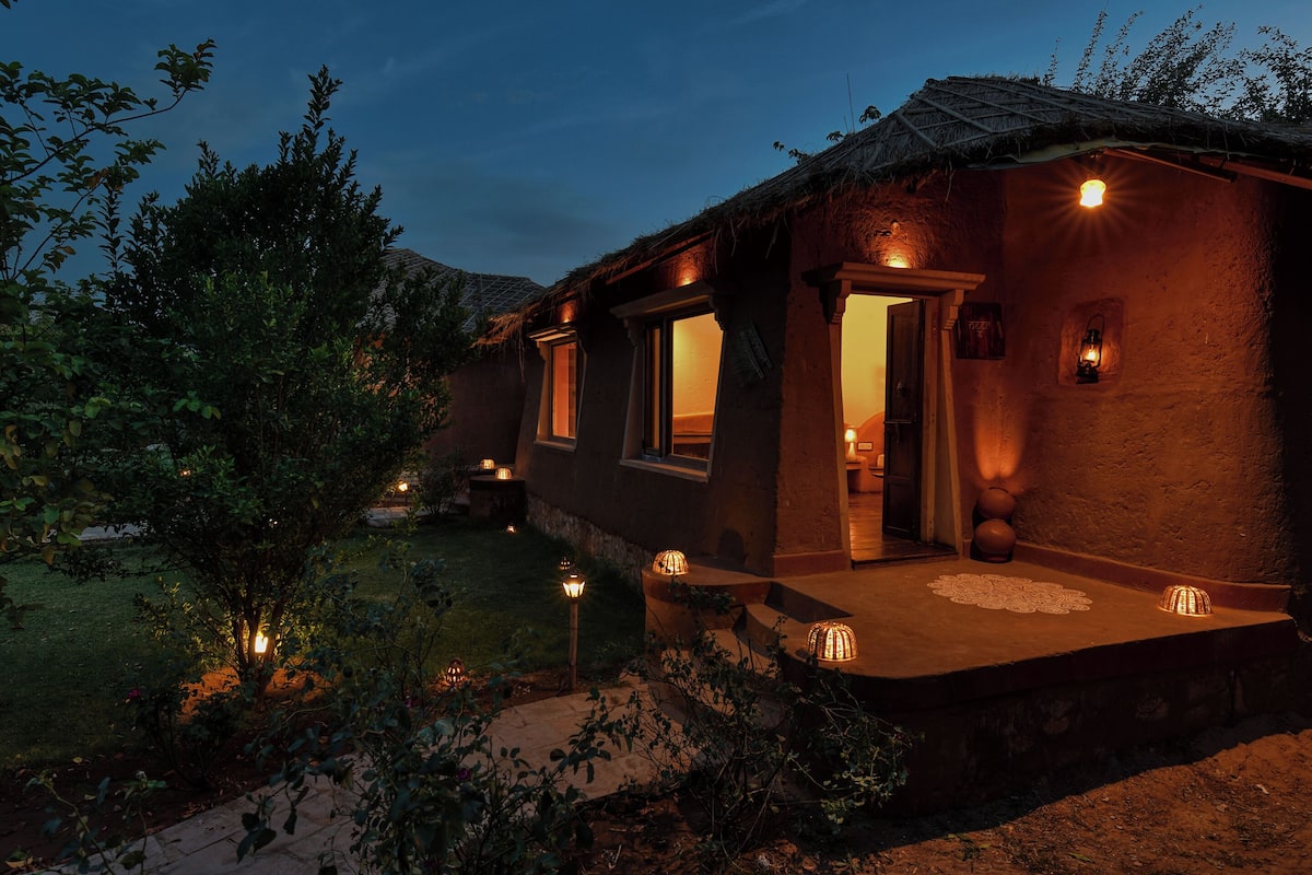 A rustic building with a thatched roof, illuminated windows, and a small porch area.