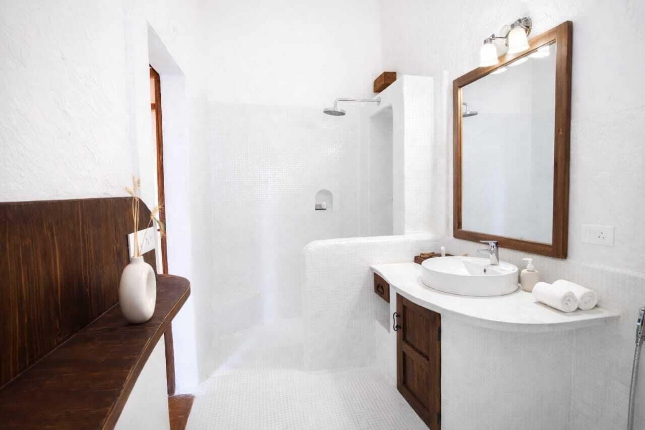 A bathroom with a wooden bench, a white sink, a large mirror, and a shower area.