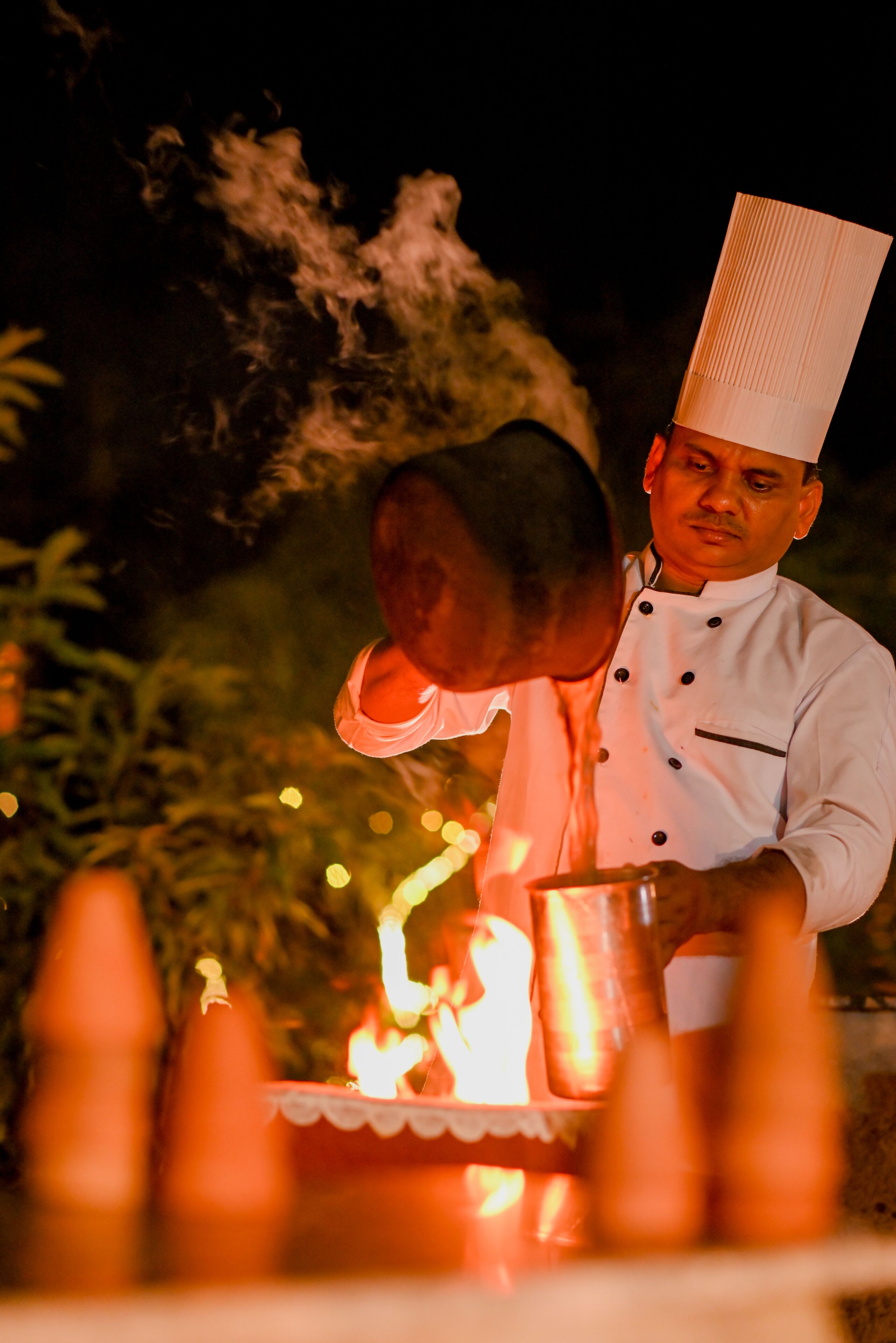 Un chef, vêtu d’un uniforme blanc, verse un liquide d’une casserole dans un récipient.