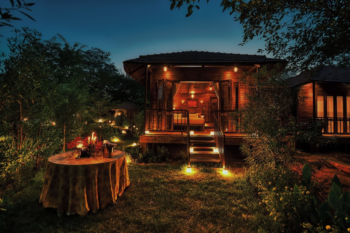 A wooden cabin with a covered porch, a dining table with candles, and a staircase leading to the upper level.