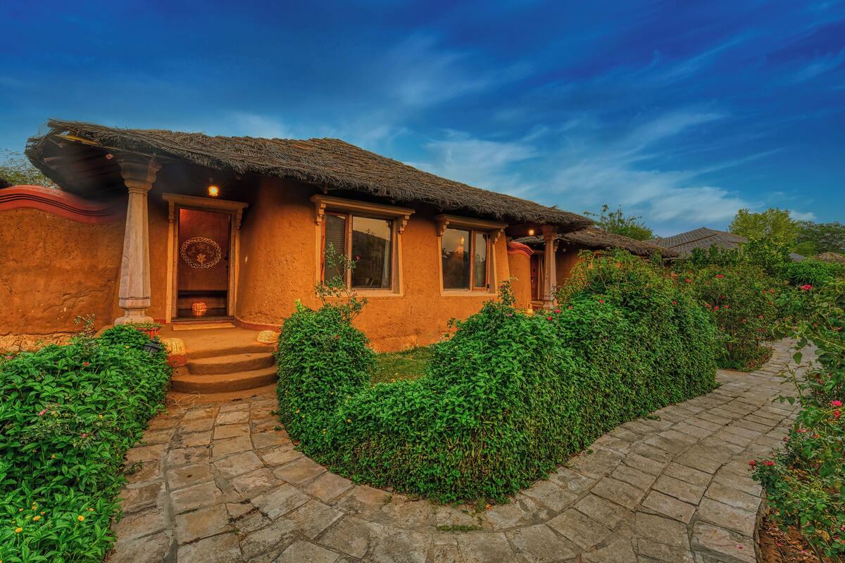 A rustic house with a thatched roof, a stone pathway, and lush greenery.