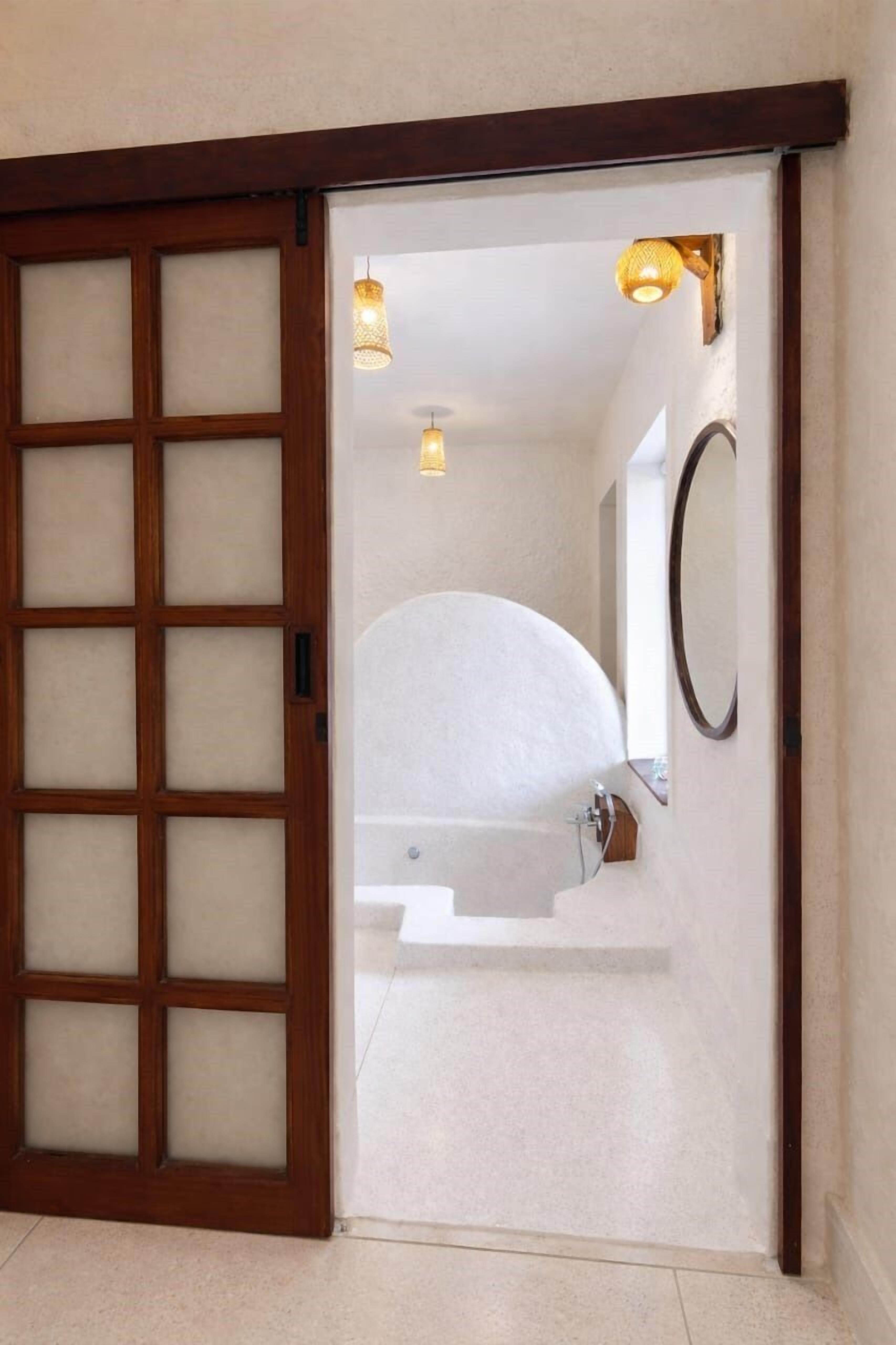 Une salle de bain avec une porte en bois, une baignoire blanche et un miroir au mur.