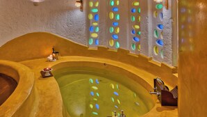 A spa with a large oval hot tub, a small rectangular hot tub, and a wall with colorful circular windows. - The Earth At Ranthambore (Sawai Madhopur)