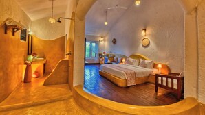 A cozy bedroom with a curved wooden bench, a bed with a headboard, and a small wooden chair. - The Earth At Ranthambore (Sawai Madhopur)