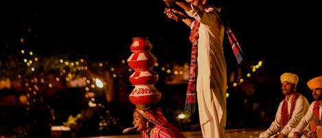 A person in traditional attire performing on a stage with a backdrop of lights.