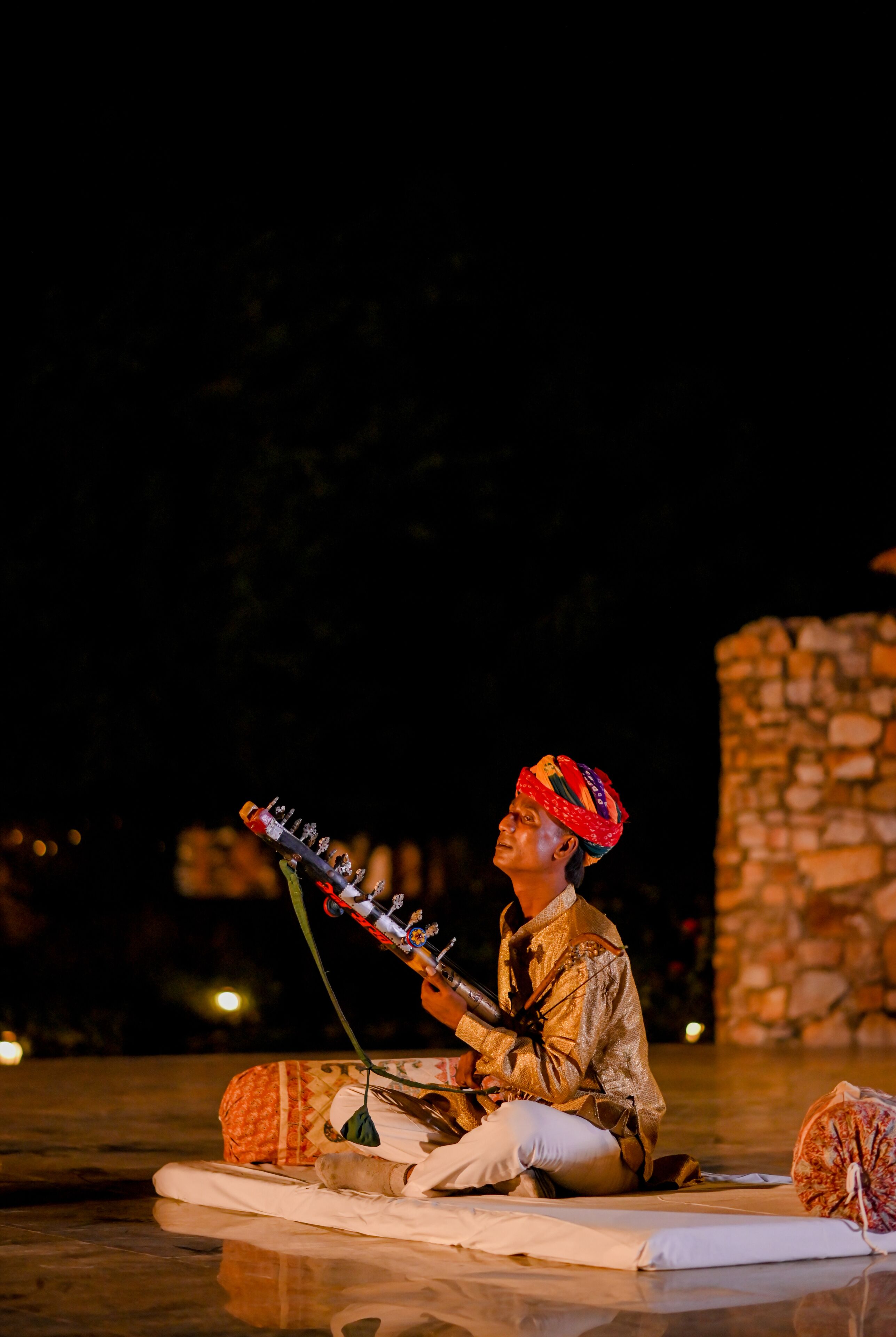 A person playing a stringed instrument on a stage with a stone wall in the background.