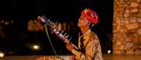 A person playing a stringed instrument on a stage with a stone wall in the background.