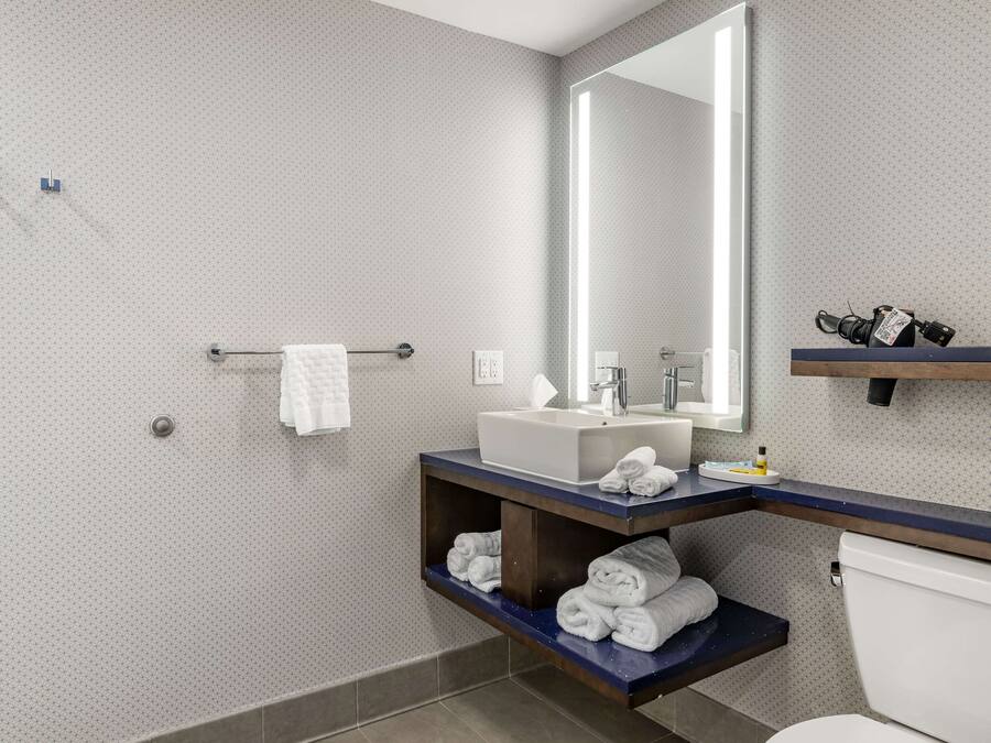 Une salle de bain moderne avec un grand miroir, un lavabo blanc et des étagères intégrées pour les serviettes.