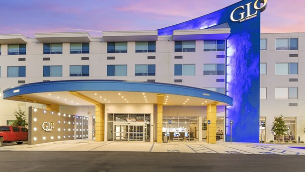A hotel entrance with a blue awning, a gated driveway, and a red vehicle parked outside.