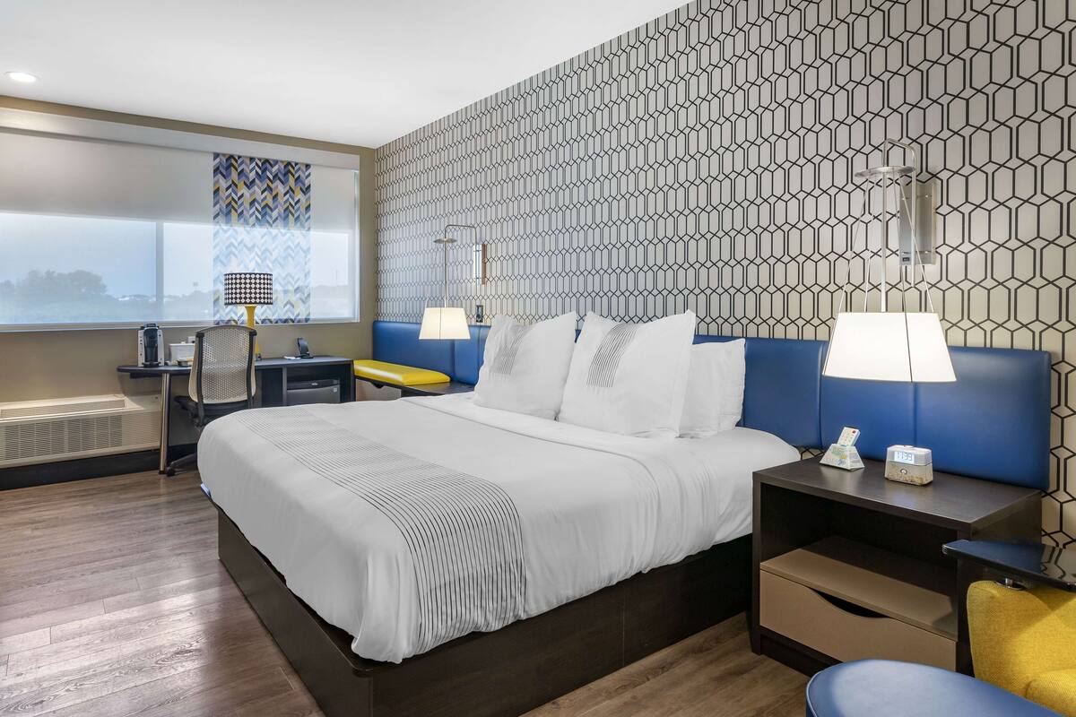 Hotellihuone, jossa on suuri sänky, työpöytä tuolilla, lamppu ja yöpöytä lampun kanssa.