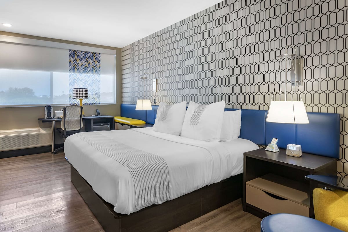 Hotellihuone, jossa on suuri sänky, työpöytä tuolilla, lamppu ja yöpöytä lampun kanssa.