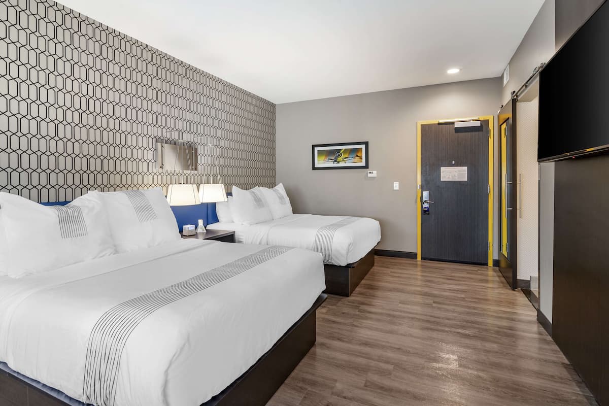 Hotellihuone, jossa on kaksi sänkyä, kuviollinen seinä, kehystetty taulu ja ovi, jossa on kyltti.