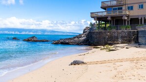 A beachfront property with a rocky shoreline, a sandy beach, and a multi-story building with balconies overlooking the ocean. - Kahana Sunset E10:  Summer and Fall Savings!  Free Activities! (Kahana)