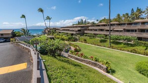 A hotel with multiple balconies overlooking a beach, a parking area, and well-maintained lawns. - Kahana Sunset E10:  Summer and Fall Savings!  Free Activities! (Kahana)